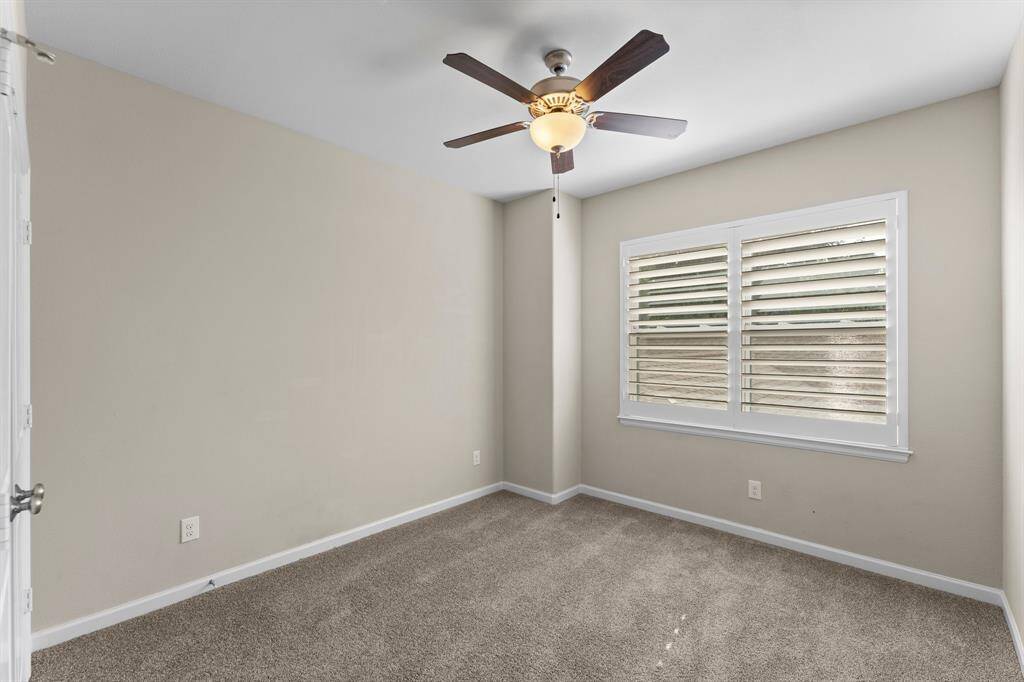 Cozy secondary bedroom features plush carpet, neutral tones, and a large window with plantation shutters for natural light.