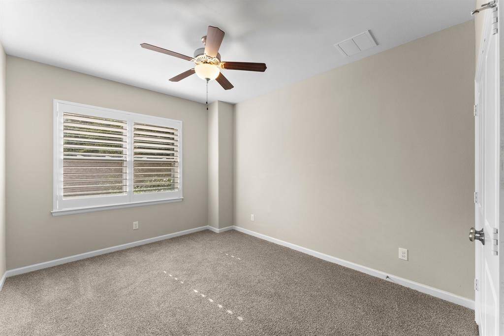 Bright secondary bedroom with plush carpeting, a ceiling fan, and a large window with plantation shutters for privacy and natural light.
