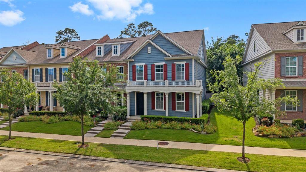 Charming two-story home with striking red shutters, a spacious front balcony, and beautifully manicured landscaping in a quiet, tree-lined neighborhood.