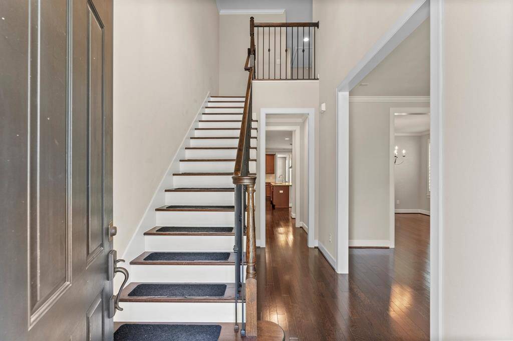 Inviting entryway features rich wood flooring, elegant staircase with wrought iron spindles, and views into the open main living areas.