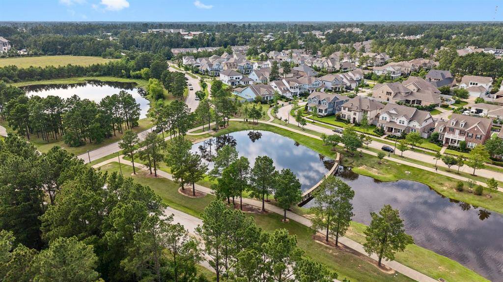 Scenic aerial view of a picturesque community featuring charming homes, tree-lined walking trails, and tranquil ponds connected by a charming footbridge.