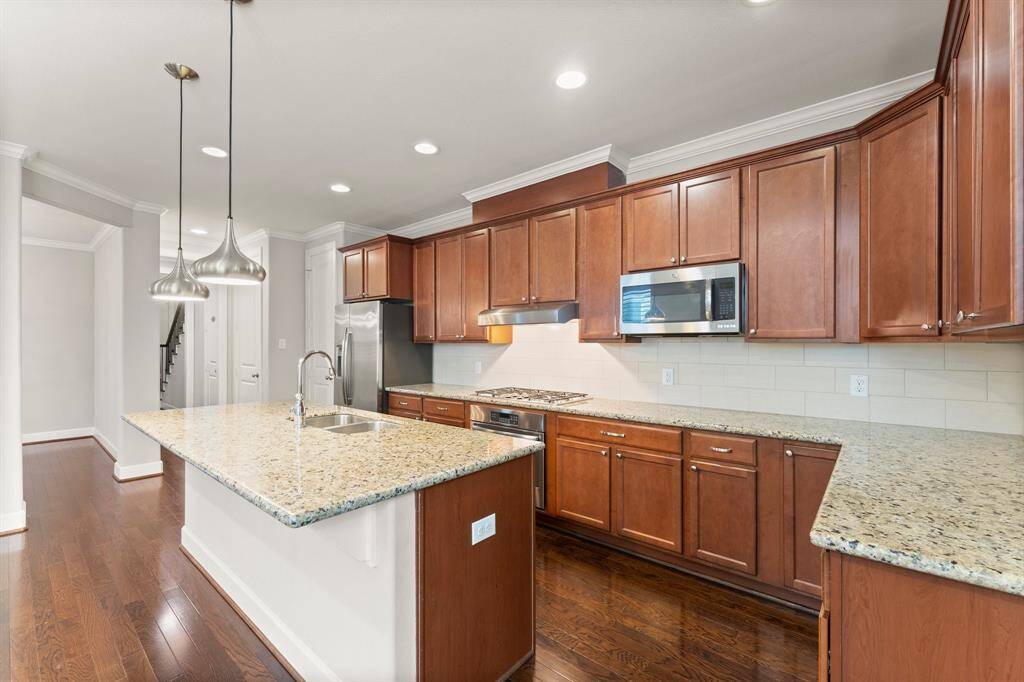 This spacious kitchen features rich wood cabinetry, granite countertops, stainless steel appliances, and a large center island with pendant lighting.