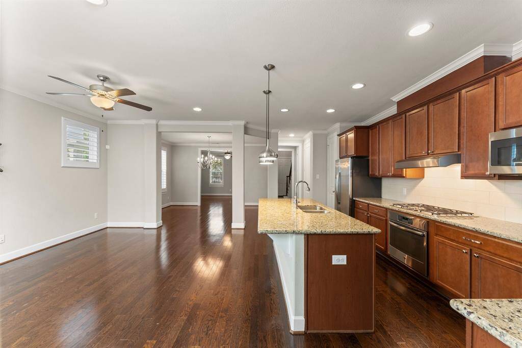 This spacious open-concept kitchen and living area features granite countertops, stainless steel appliances, rich wood cabinetry, and hardwood floors throughout.