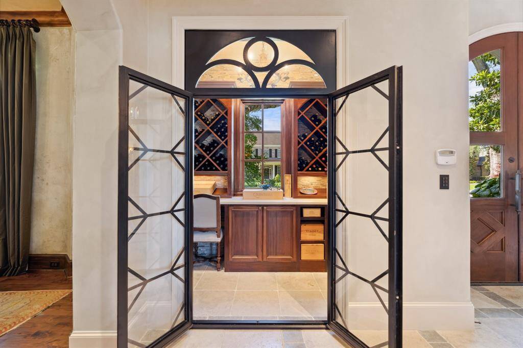 Wine Room with Wrought iron and glass double doors. The room also features Built-in wine storage, Honed limestone countertops, and a U-Line Wine Cooler.
