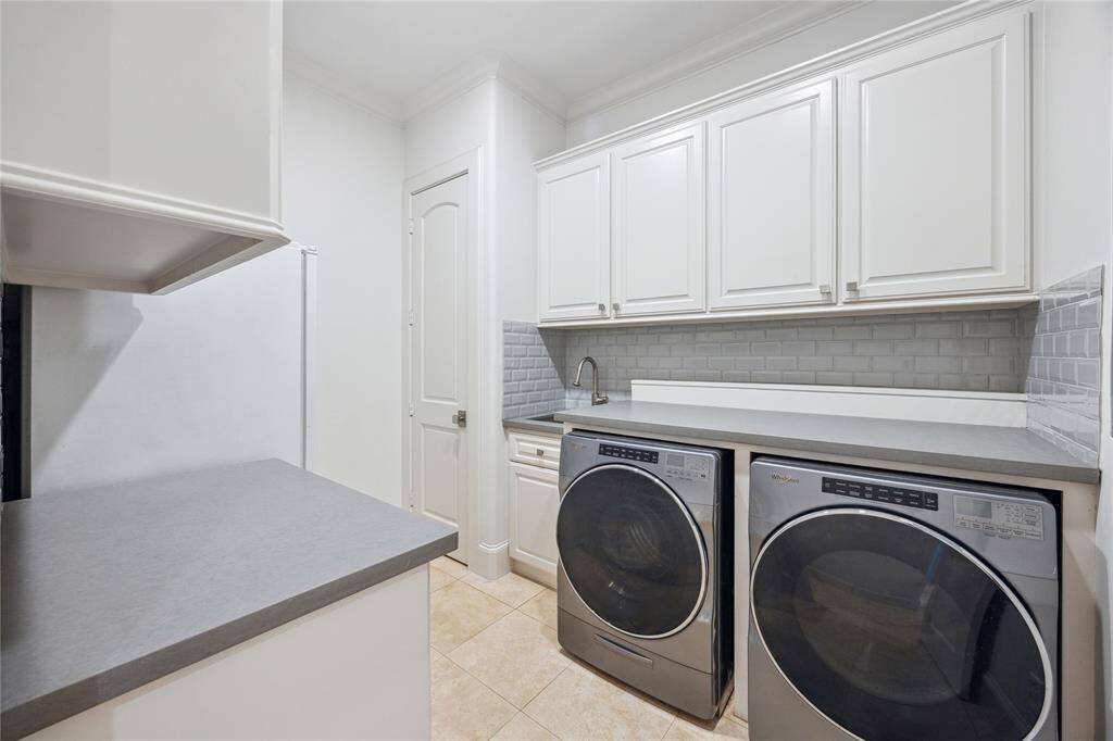 This thoughtfully designed laundry room features built-in cabinetry throughout, a quartz countertop with custom inserts for the washer and dryer, and a stainless steel sink.