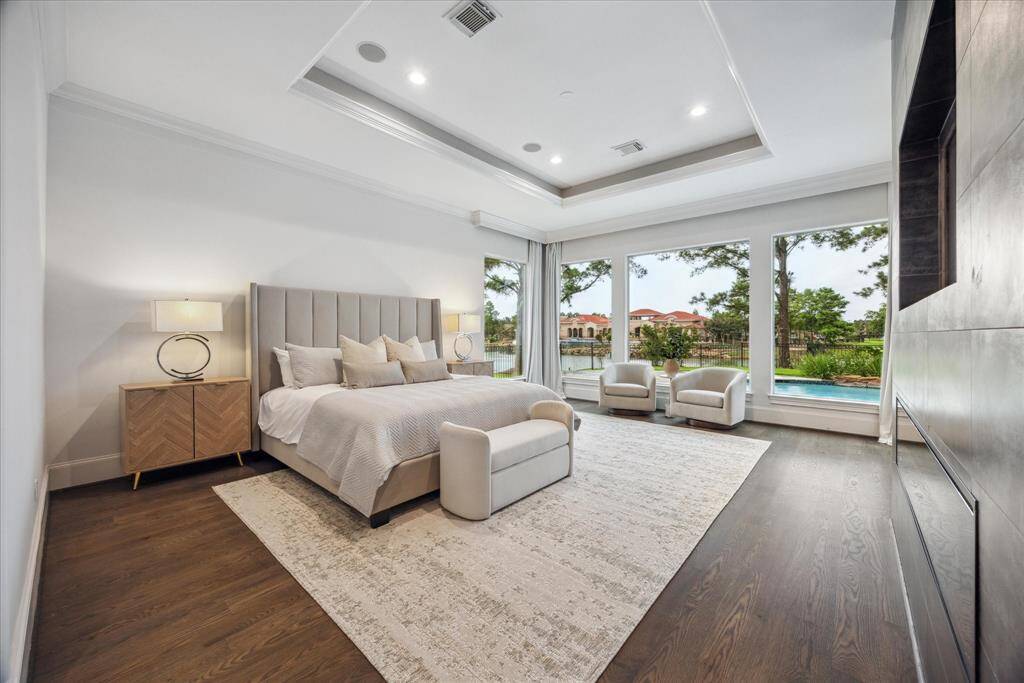 The spacious primary bedroom offers stunning lake and pool views through large windows dressed with custom valances. Featuring rich oak flooring.