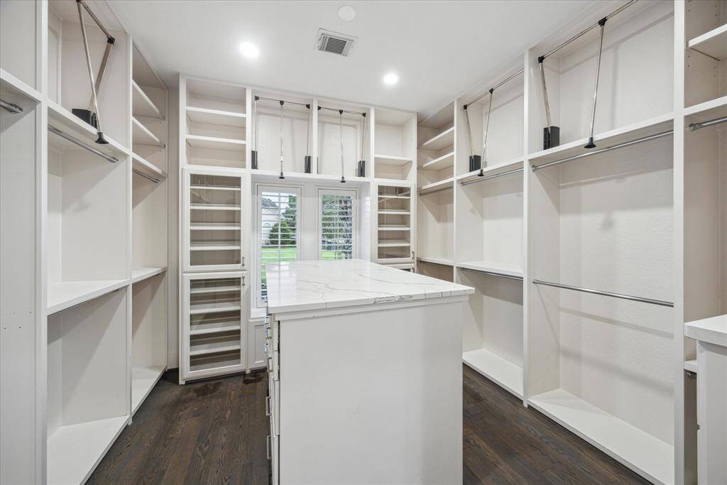 The expansive primary closet features rich oak flooring, a central island with quartz countertop and oversized drawers, additional hanging space, and built-in cabinetry.
