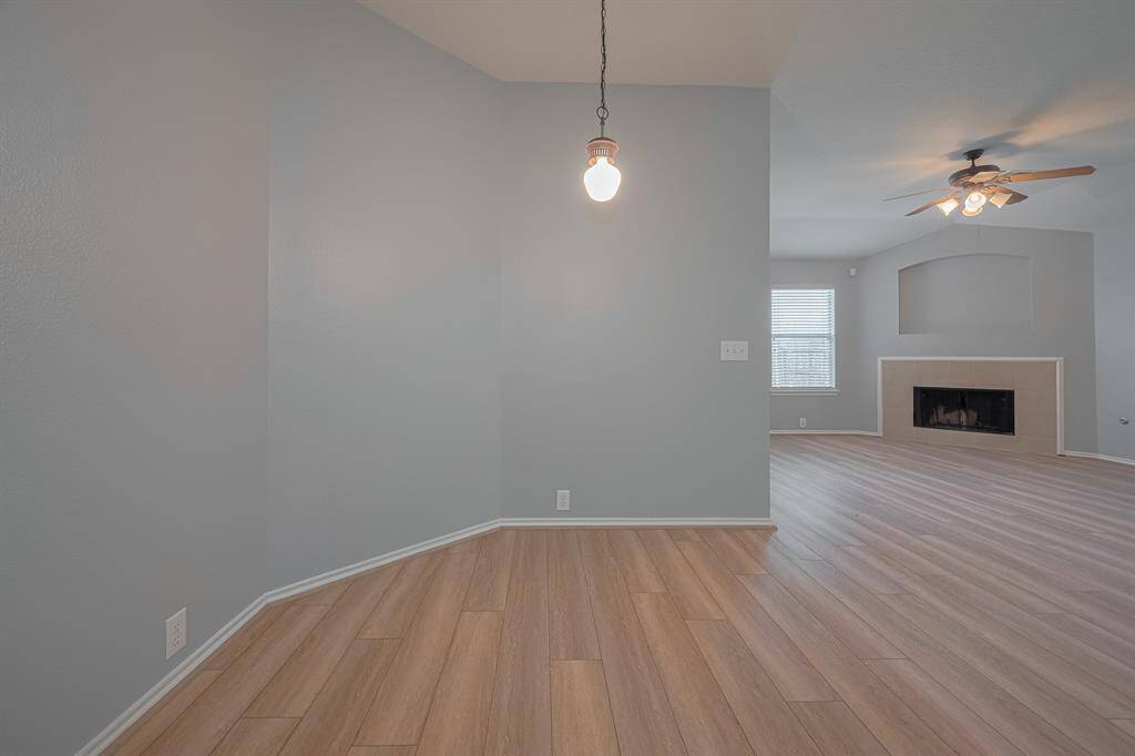 This photo showcases a spacious room with light wood flooring and soft gray walls. It features a ceiling fan, a modern light fixture, for a adjoining breakfast area, creating a warm, inviting atmosphere.