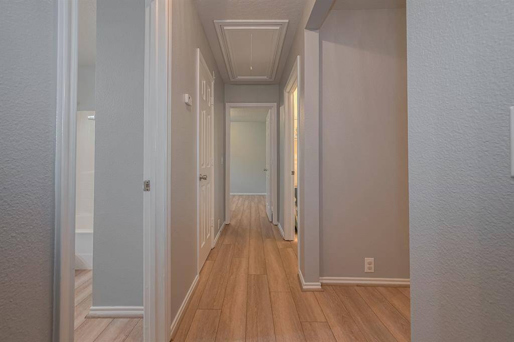 This photo shows a clean, well-lit hallway with light wood flooring and neutral wall colors. There are multiple doors leading to other rooms, creating a spacious and inviting feel.