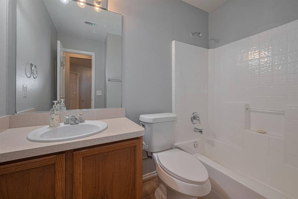 This is a clean, modern hall bathroom featuring a vanity with a sink, a large mirror, and a combination bathtub and shower with white tiles. The neutral color scheme adds a fresh and inviting feel.