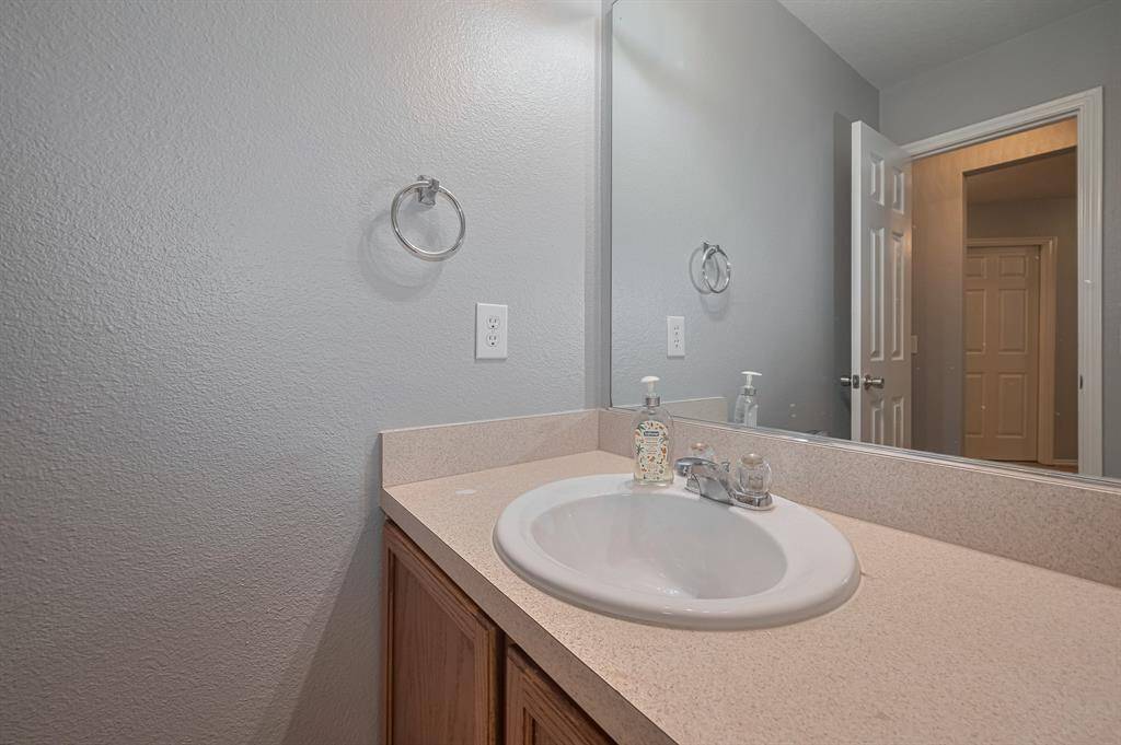 This photo shows a clean, modern bathroom with a beige countertop, a single sink, and a large mirror. The soft gray walls create a calming atmosphere, and there's ample lighting.