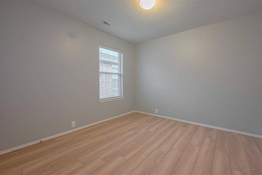 This is a bright, room with light hardwood flooring and soft gray walls. It features a ceiling light fixture and a window that allows natural light to enter, creating a welcoming atmosphere.