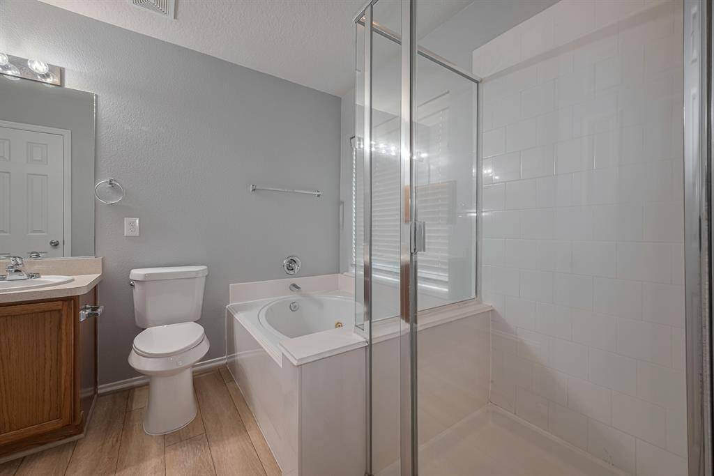 This primary bathroom features a modern design with a glass-enclosed shower, a separate bathtub, a single-sink vanity with a wooden cabinet, and neutral walls and flooring for a clean, bright look.