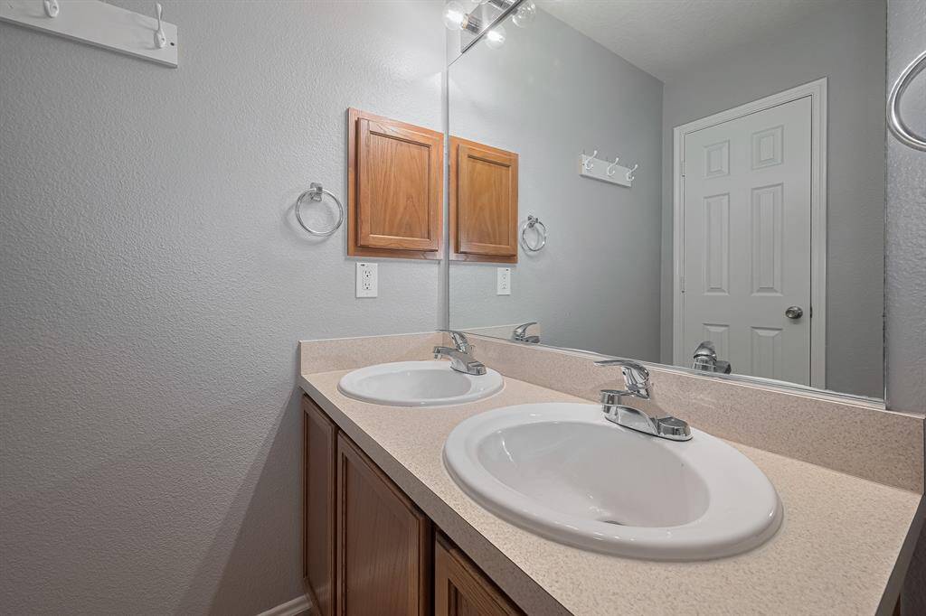 This bathroom features a dual-sink vanity with a large mirror, wooden cabinets, and modern fixtures, providing ample space and functionality.