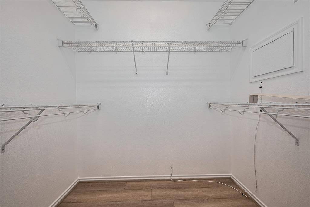 Spacious walk-in closet with white walls, featuring multiple wire shelves for ample storage. The flooring is a light wood finish, adding warmth to the space. Ideal for organizing clothes and accessories.