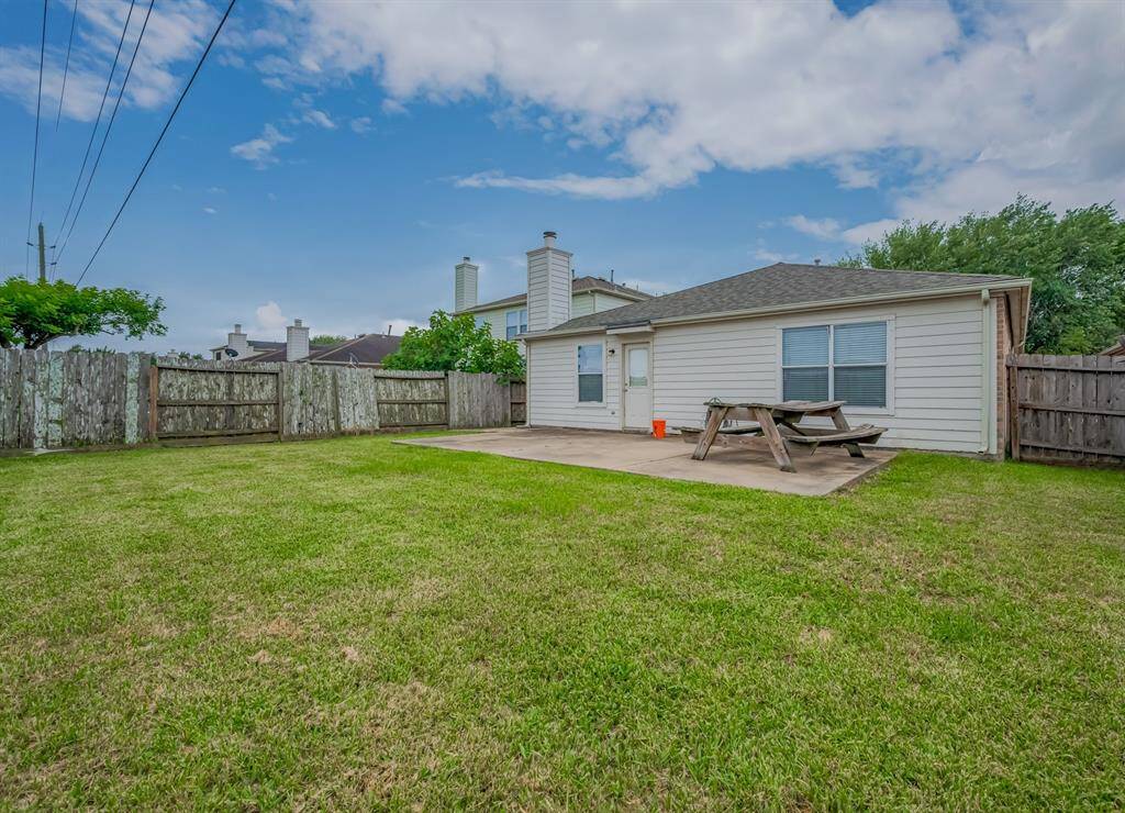 This backyard features a spacious grassy area, a patio with a picnic table, and is enclosed by a wooden fence, offering privacy and outdoor enjoyment.