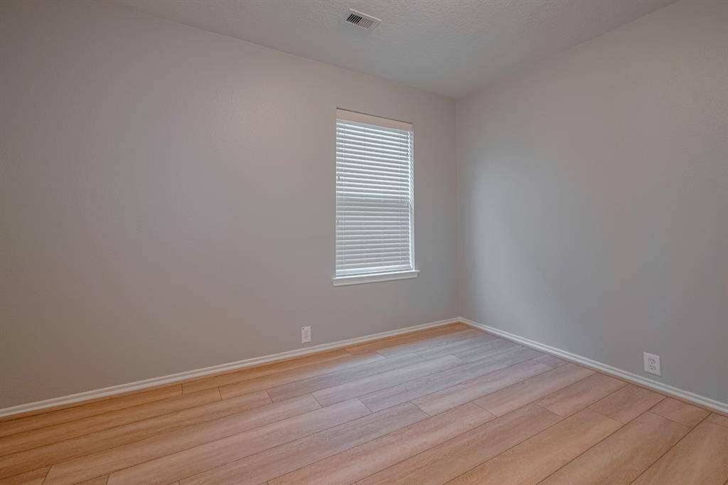 This is a secondary bedroom with wood-style flooring. It features a single window with blinds, allowing natural light to enter.
