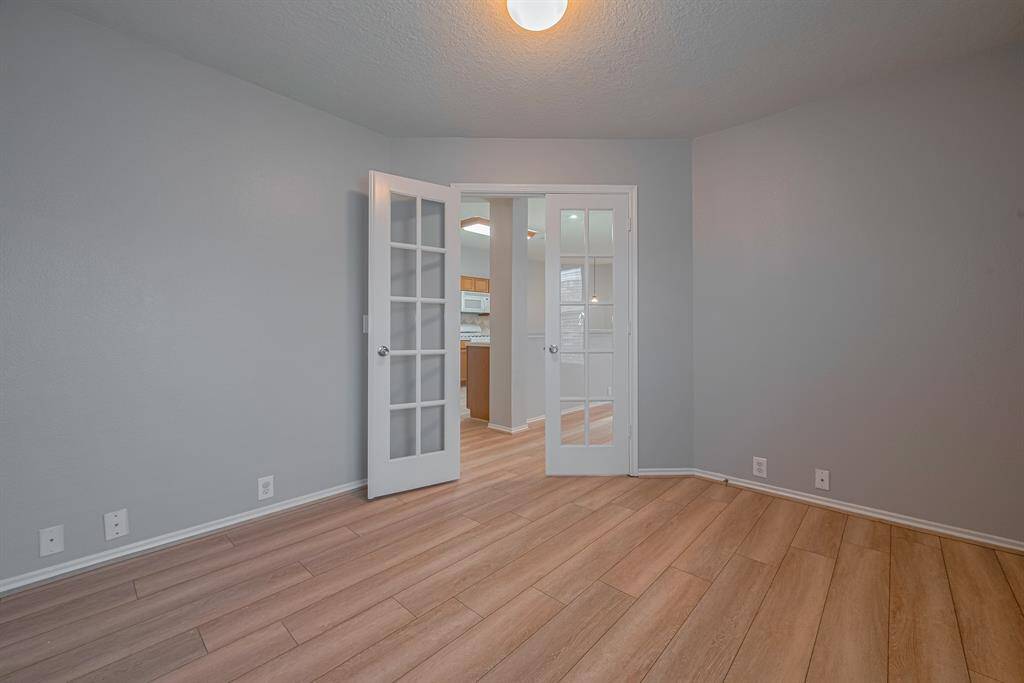 This room features light wood flooring, neutral gray walls, and French doors leading to another space. It has a modern, clean look with ample natural light, ideal for a home office or extra bedroom.