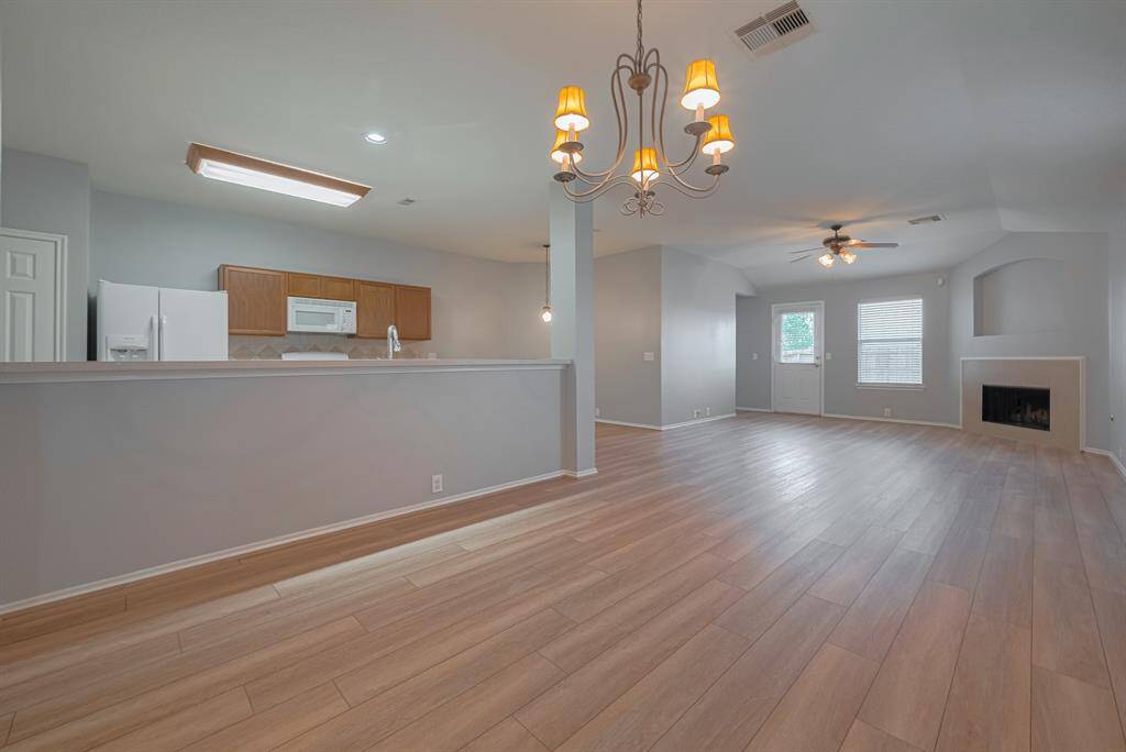 This spacious open-plan living area features light wood flooring, a cozy fireplace, and a modern kitchen with a breakfast bar. Natural light fills the room, enhanced by stylish lighting fixtures. Ideal for entertaining and family living.