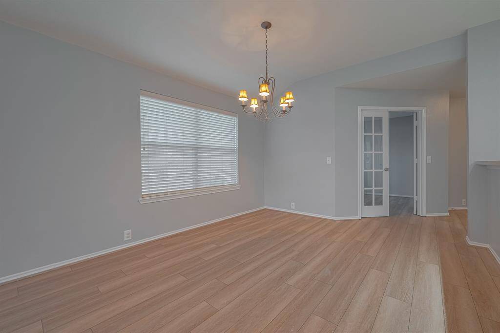 Bright dining area with light wood flooring, soft gray walls, and a modern chandelier. Features a large window with blinds and French doors leading to another room. Perfect for entertaining.
