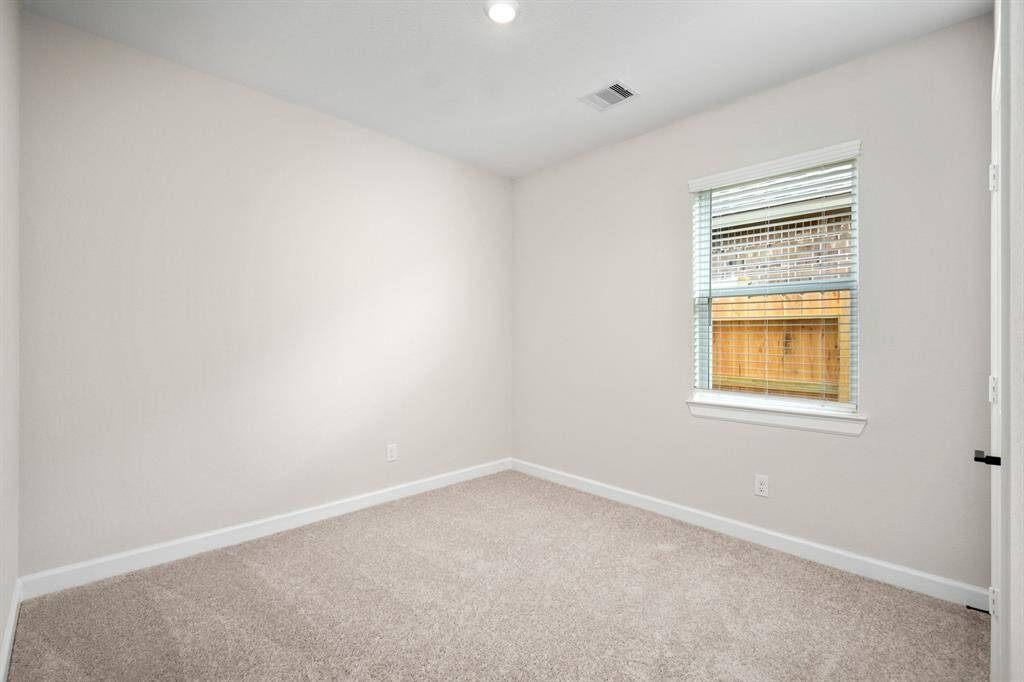 The secondary bedroom has a large window and comfortable carpet flooring.