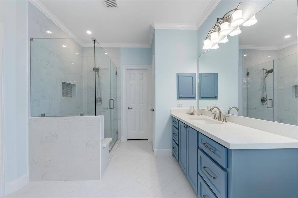 Beautifully appointed primary bath featuring a frameless glass shower, dual sinks, and custom cabinetry in a serene blue hue.