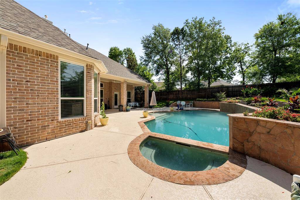 View of the custom pool and attached spa from the patio side—lush greenery adds a private, resort-like feel