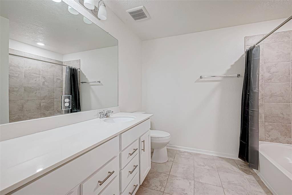 This spotless full bathroom features a long vanity with plenty of counter space and storage, perfect for busy mornings. Neutral tile floors and a tiled tub/shower combo complete the space with style and function.