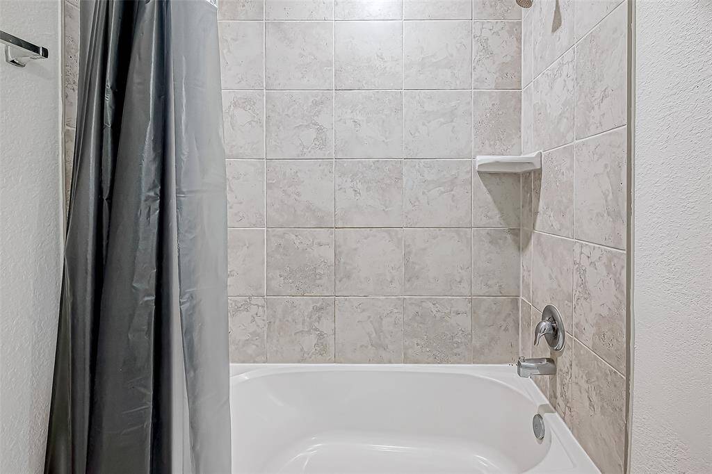 The tiled tub/shower combo offers both comfort and convenience, with a clean, modern look and built-in shelving to keep bath essentials close at hand.