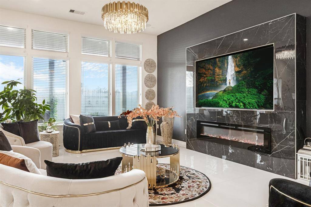 Living room features tile flooring, achandelier, high ceilings, cozy fireplace, accent wall, and a wallof windows.