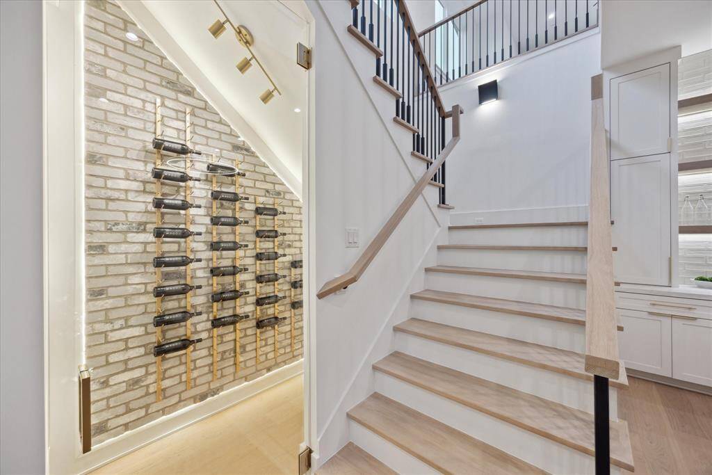 [WINE ROOM] Tucked gracefully beneath the staircase, the custom wine room is a stunning use of space, combining form and function with French contemporary flair. Featuring wall-mounted wine racks set against a textured brick backdrop, this thoughtfully designed nook offers both visual charm and practical storage—perfect for displaying your favorite vintages in style.
