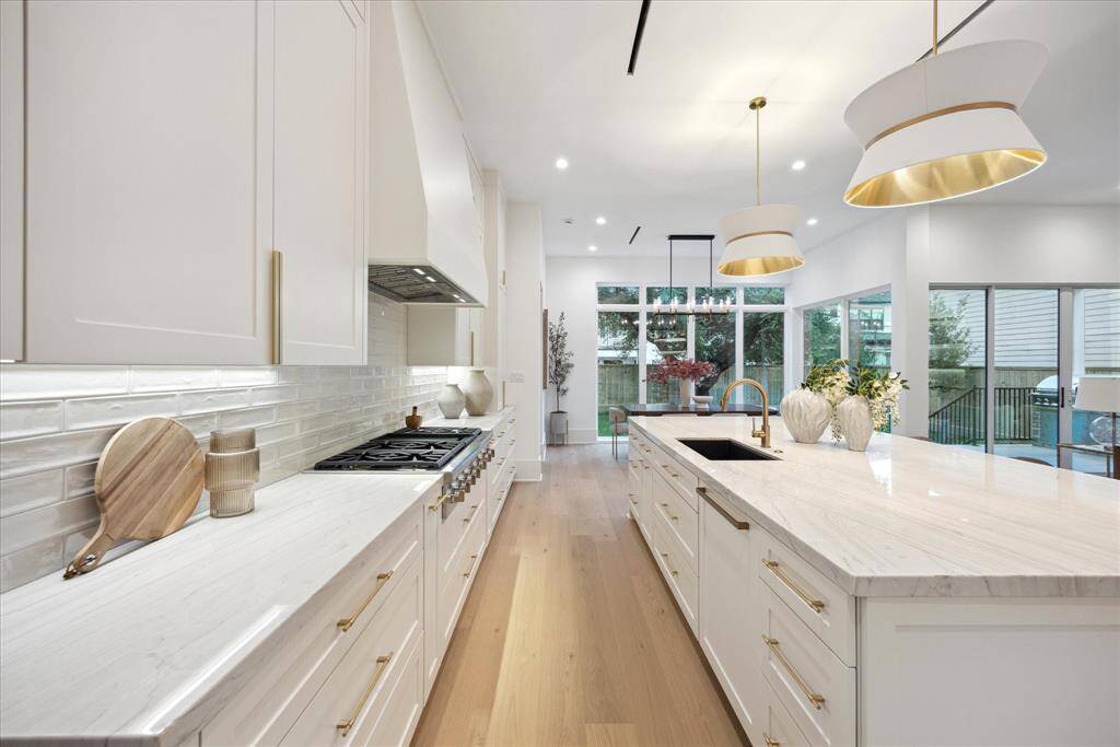 The stylish kitchen centers around a large, inviting island adorned with stunning pendant lighting, creating a perfect gathering spot for cooking and conversation. Under-cabinet lighting highlights the elegant countertops and enhances the warm, inviting atmosphere.