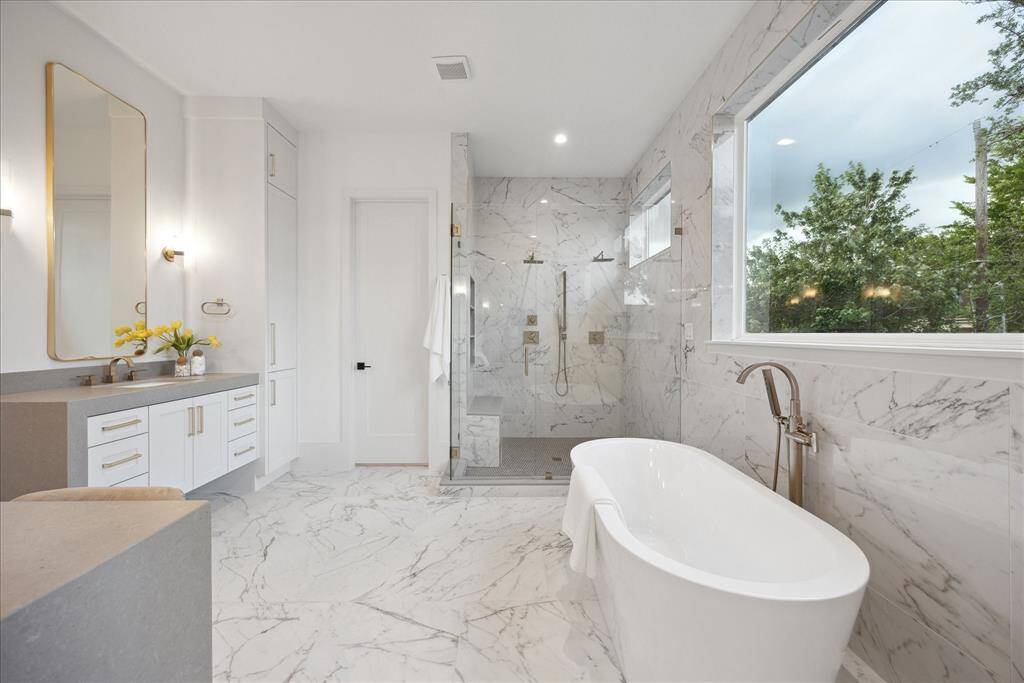 [PRIMARY BATHROOM] This spa-inspired primary bathroom is a haven of tranquility and refined elegance. Designed with impeccable attention to detail, it showcases stunning finishes, rich natural stone surfaces, and designer hardware.