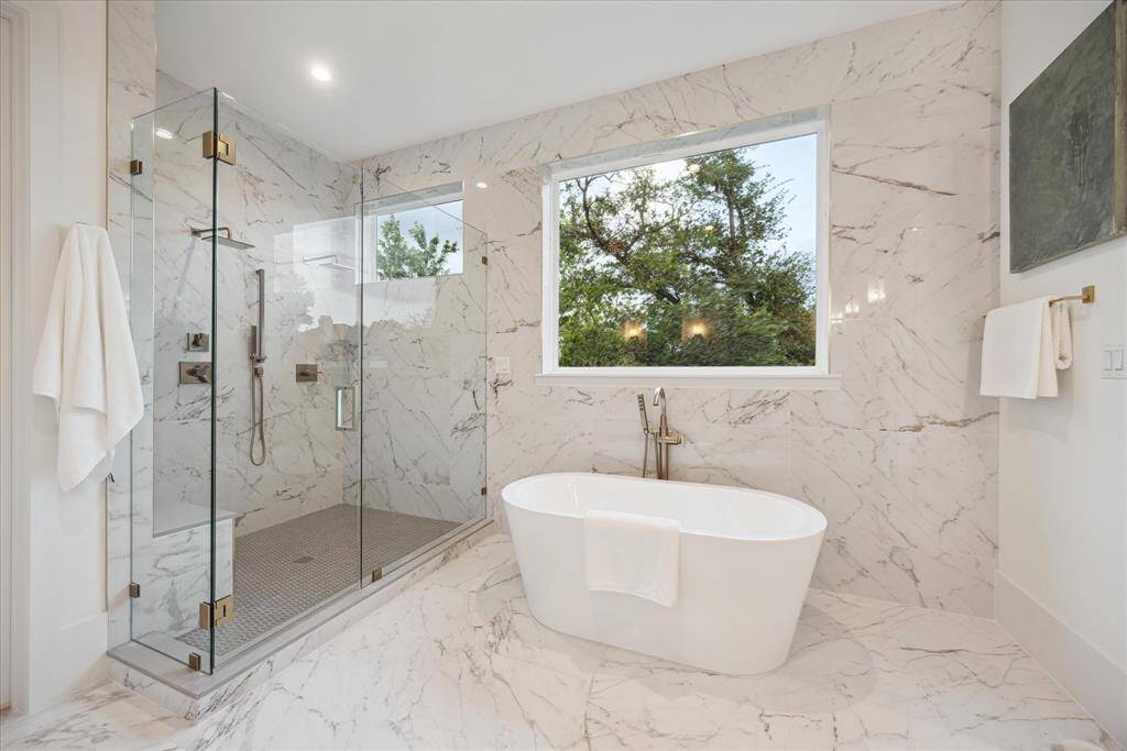 A sculptural freestanding tub invites relaxation, while the expansive walk-in shower with frameless glass enclosure completes this spa-like retreat, all within the refined elegance of French contemporary design.