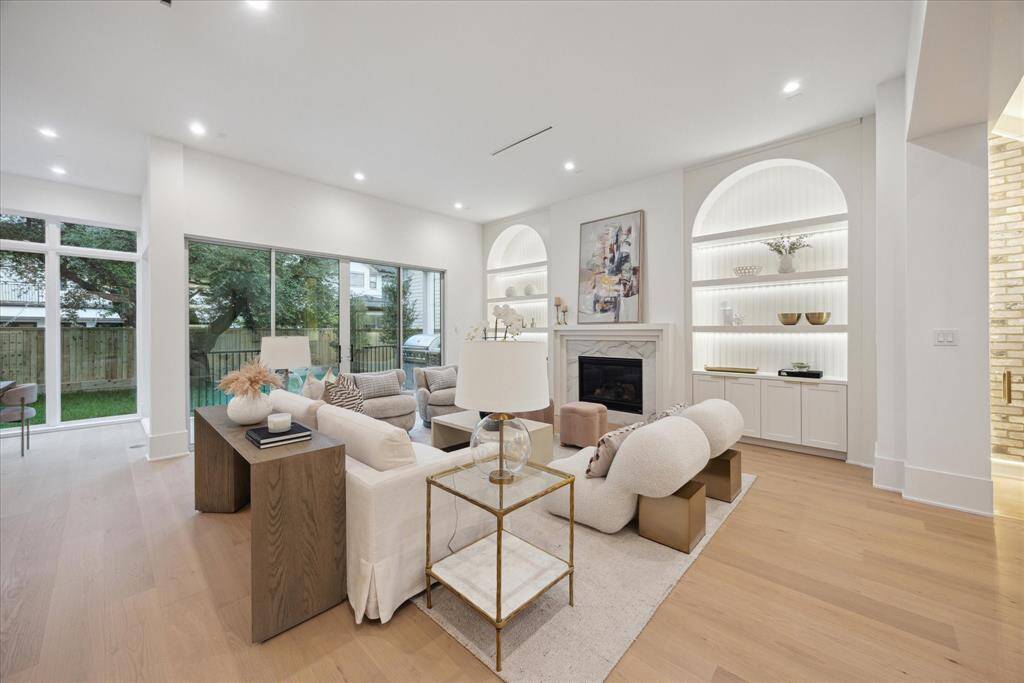 [FAMILY ROOM] The open-concept family room is the heart of the home, featuring a beautifully framed fireplace flanked by arched display shelves with integrated lighting—perfect for showcasing art or treasured collections. A wall of large windows floods the space with natural light  creating a welcoming atmosphere ideal for both everyday living and sophisticated entertaining.