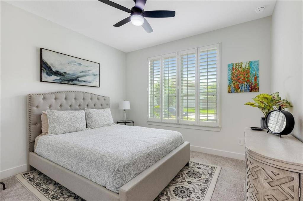 A guest bedroom on the main floor features plush carpeting, plantation shutters, and is conveniently located next to a private full bathroom—perfect for an office or mother-in-law suite.