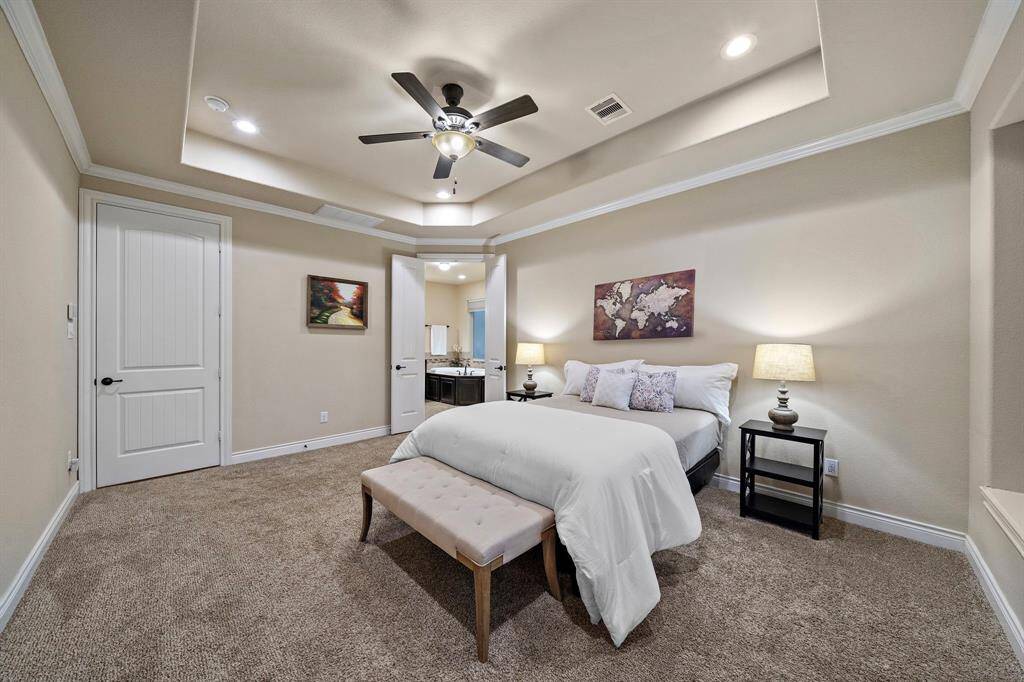 Crowned by tray ceilings with recessed lighting, the first-floor primary bedroom offers a spacious retreat finished with detailed millwork and plush carpeting underfoot.