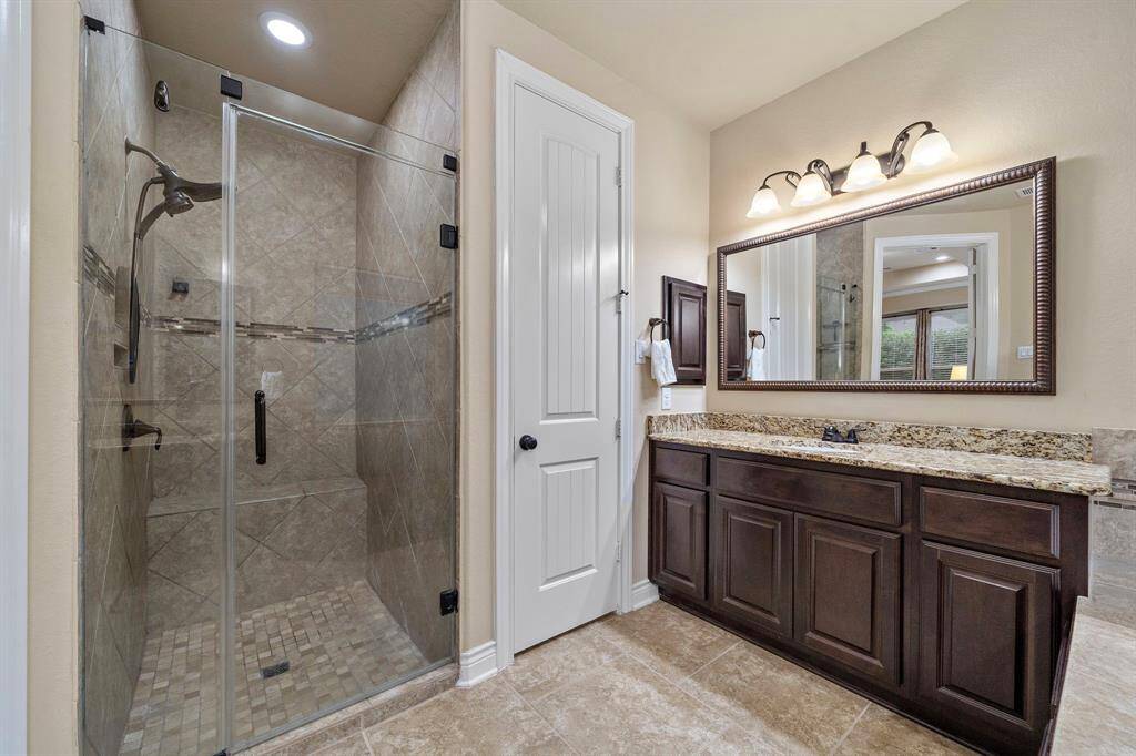 A frameless glass shower with tile surround complements the granite vanity, completing a bath that blends refinement with everyday utility.