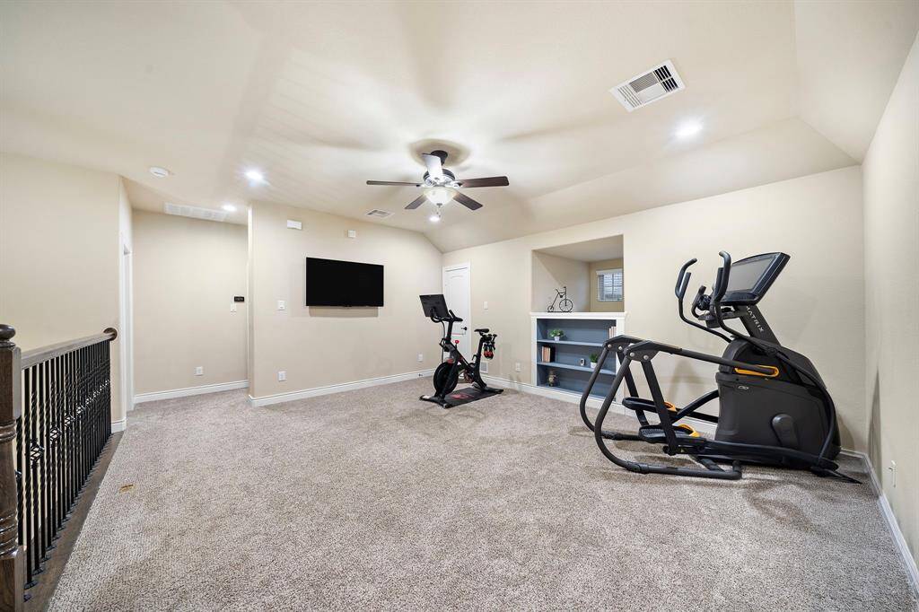 This versatile upstairs space offers ample room for recreation, fitness, or media use, with plush carpeting and built-in shelving adding comfort and functionality.