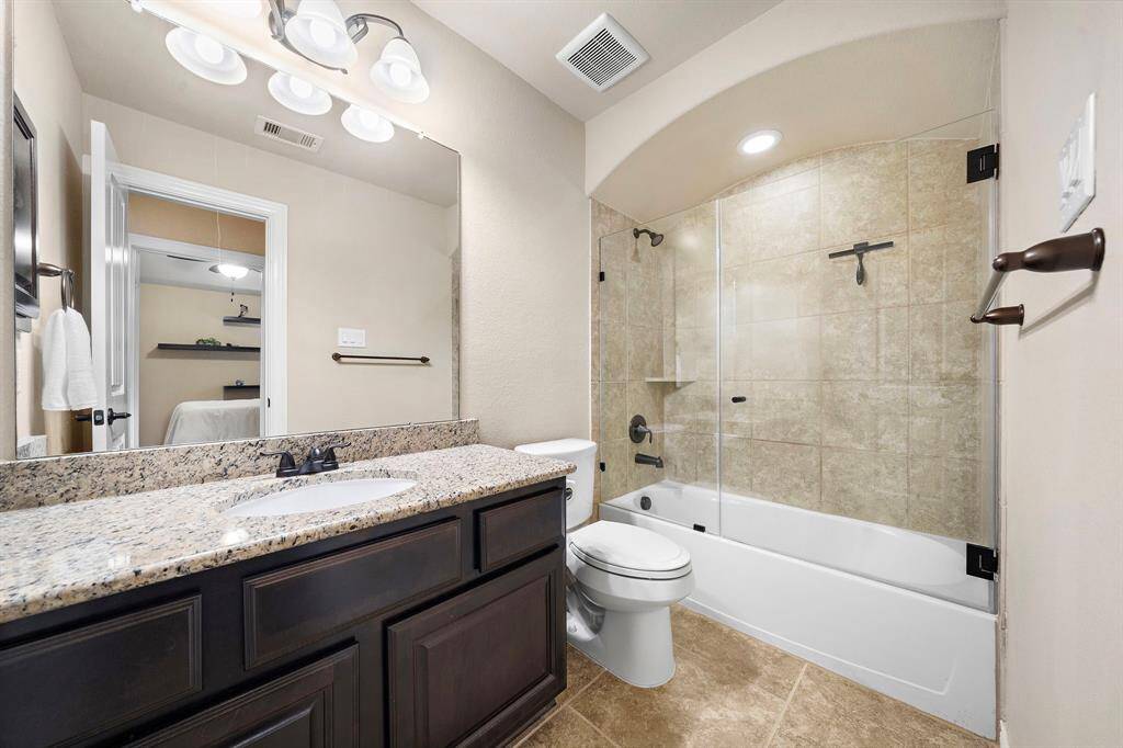 A granite counter and built-in storage bring utility and finish to the ensuite bath, paired with a tile-surround tub and frameless glass for lasting appeal.