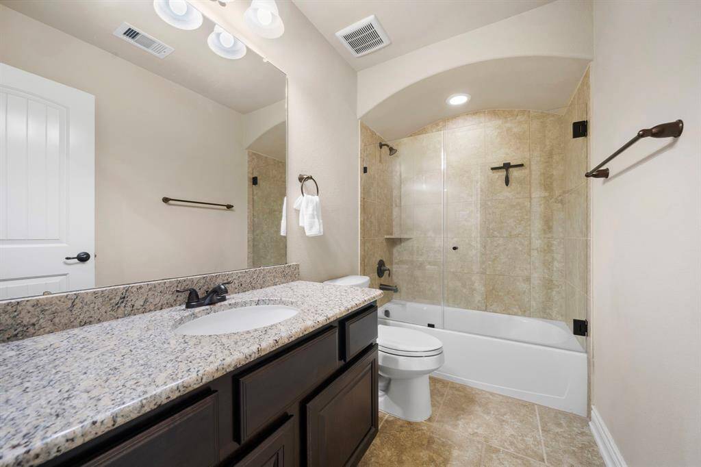 Granite countertops and brushed hardware bring a cohesive finish to the ensuite bath, featuring a glass-paneled shower and full tile surround.