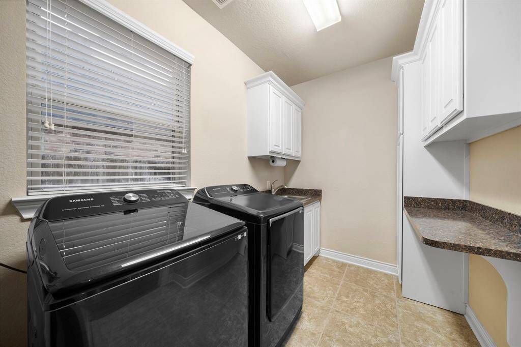 Spacious laundry room features built-in cabinets, utility sink, and generous folding area for easy sorting and organization. Tile flooring and dedicated counter space provide practicality, while upper and lower cabinetry keep essentials neatly tucked away.
