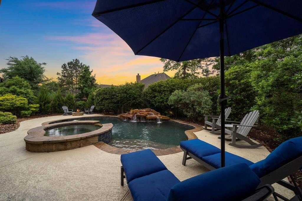 The saltwater pool and elevated spa form a striking focal point, with cascading rock elements and stone coping creating a polished, resort-style setting framed by lush greenery.