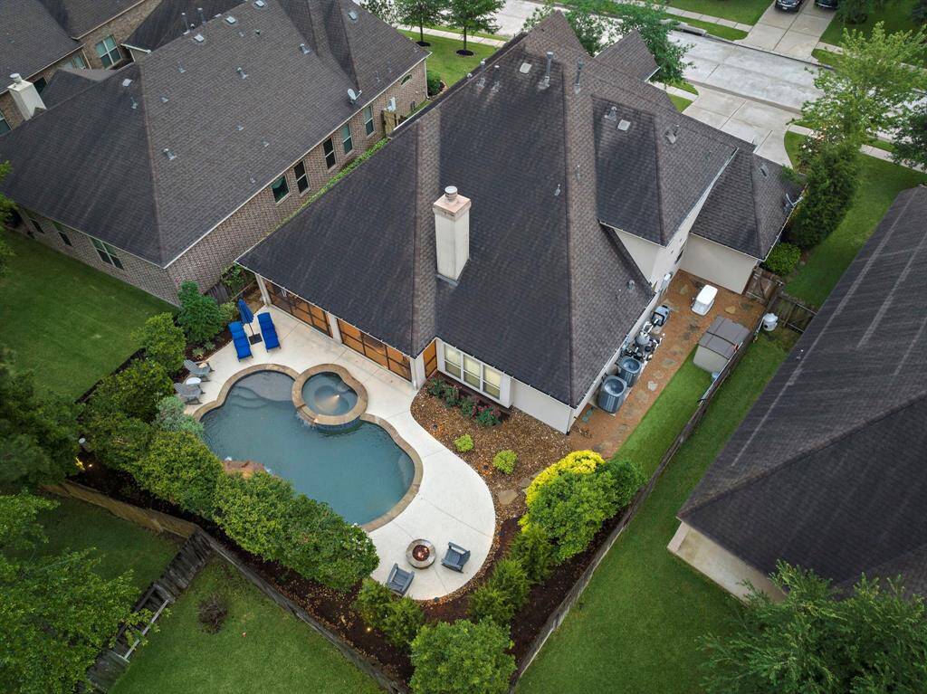 This aerial view showcases the thoughtfully designed backyard retreat featuring a saltwater pool, spa, and screened-in patio, with lush landscaping providing added privacy.
