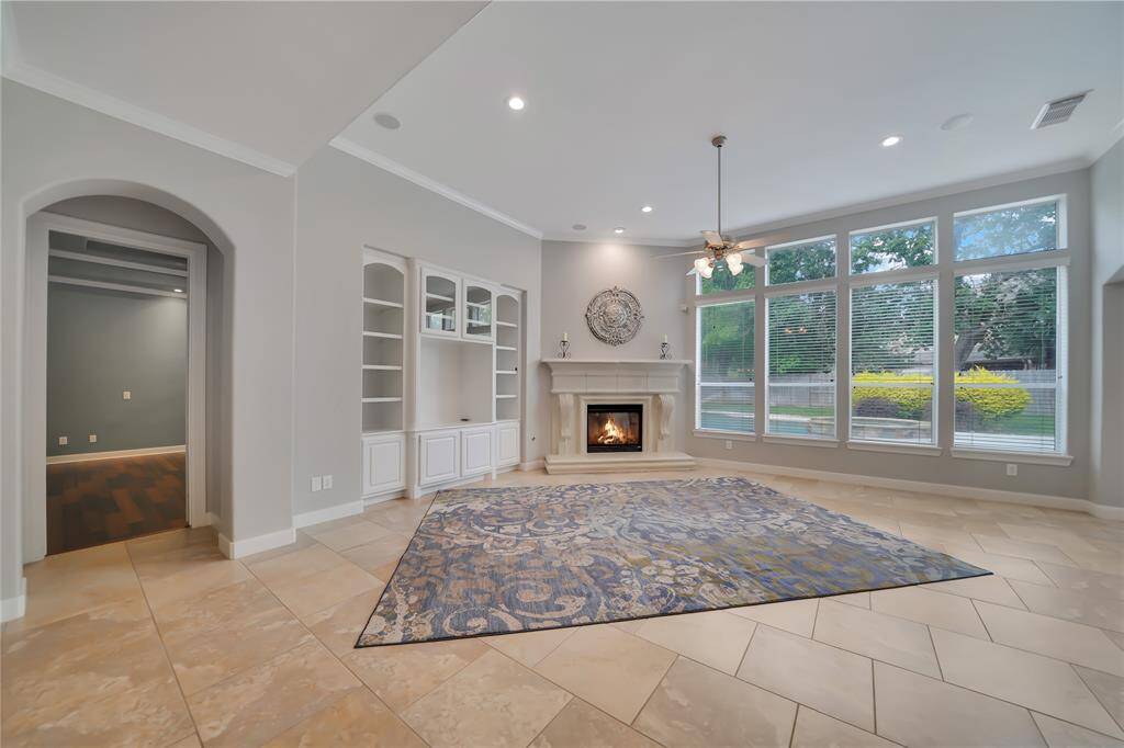 This spacious family room features a cozy fireplace, built-in shelving, and large windows offering abundant natural light and views of the backyard create a warm and inviting atmosphere.