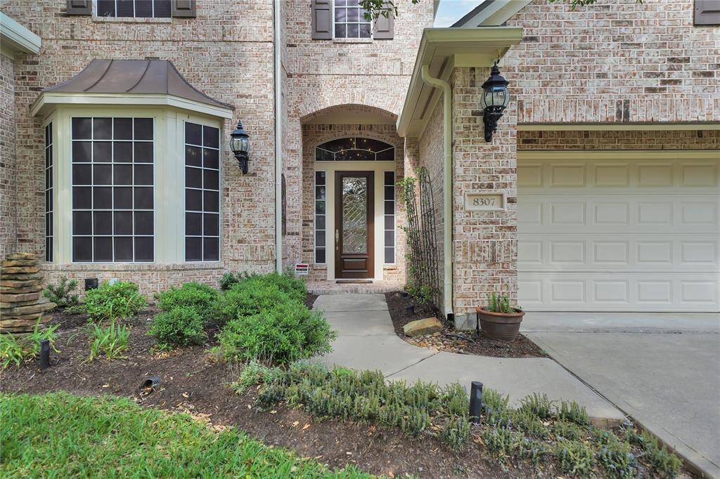 Charming brick home with a welcoming front entrance, featuring a decorative arched doorway and large bay window. The well-maintained landscaping adds curb appeal, and the 3 car attached garage provides convenient access.