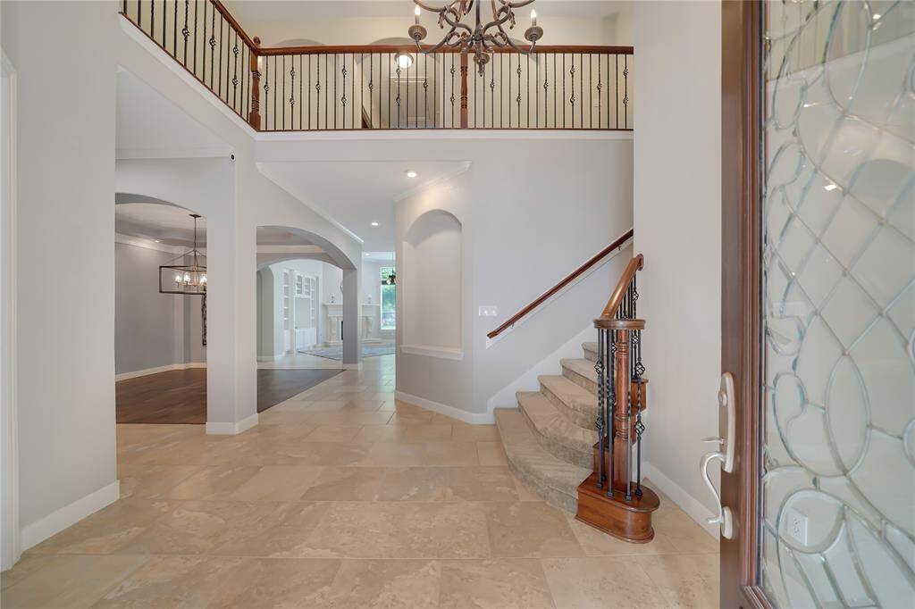 This elegant entryway features high ceilings, a grand staircase with wrought iron railings, and a spacious, open layout. The neutral tile flooring and soft lighting create a warm, inviting atmosphere, leading to a well-designed living area.