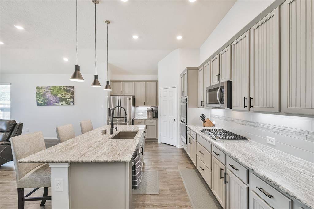 This photo showcases a modern kitchen with elegant gray cabinetry, granite countertops, and stainless steel appliances. The space features a large island with pendant lighting and ample seating, creating a bright and inviting atmosphere perfect for cooking and entertaining.