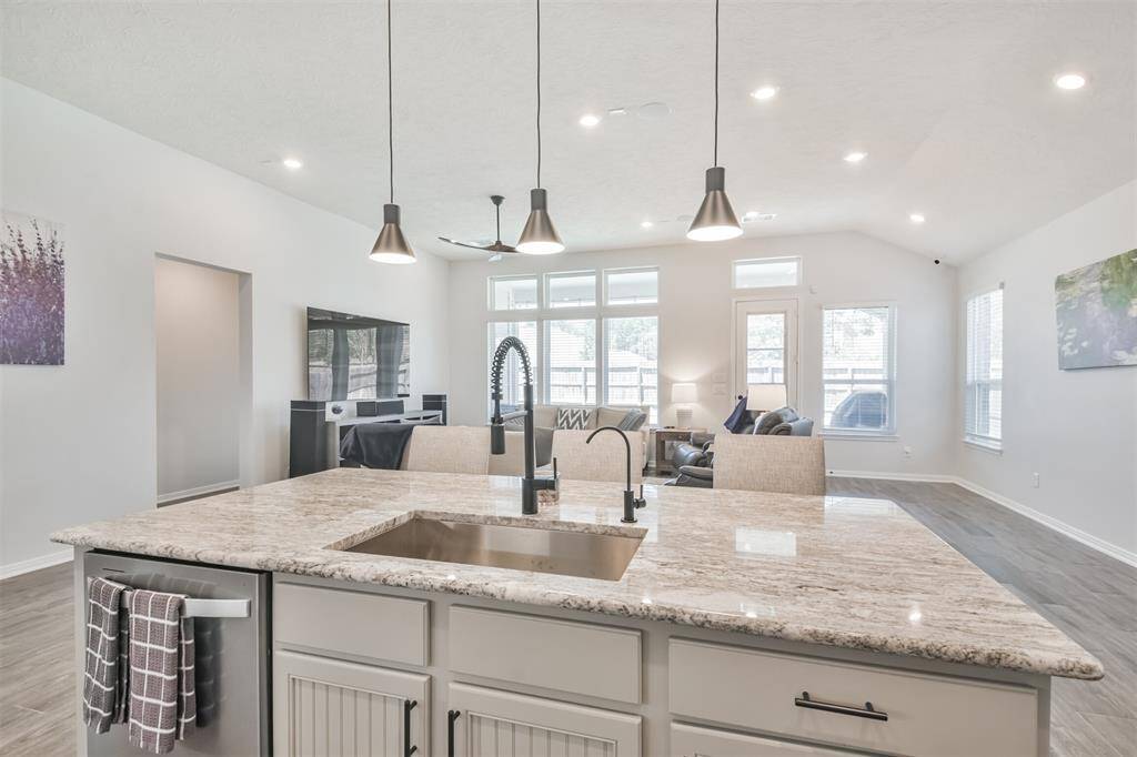 This spacious, open-concept living area features a modern kitchen with a large island and granite countertops, seamlessly flowing into a bright living room with ample natural light and contemporary lighting fixtures.