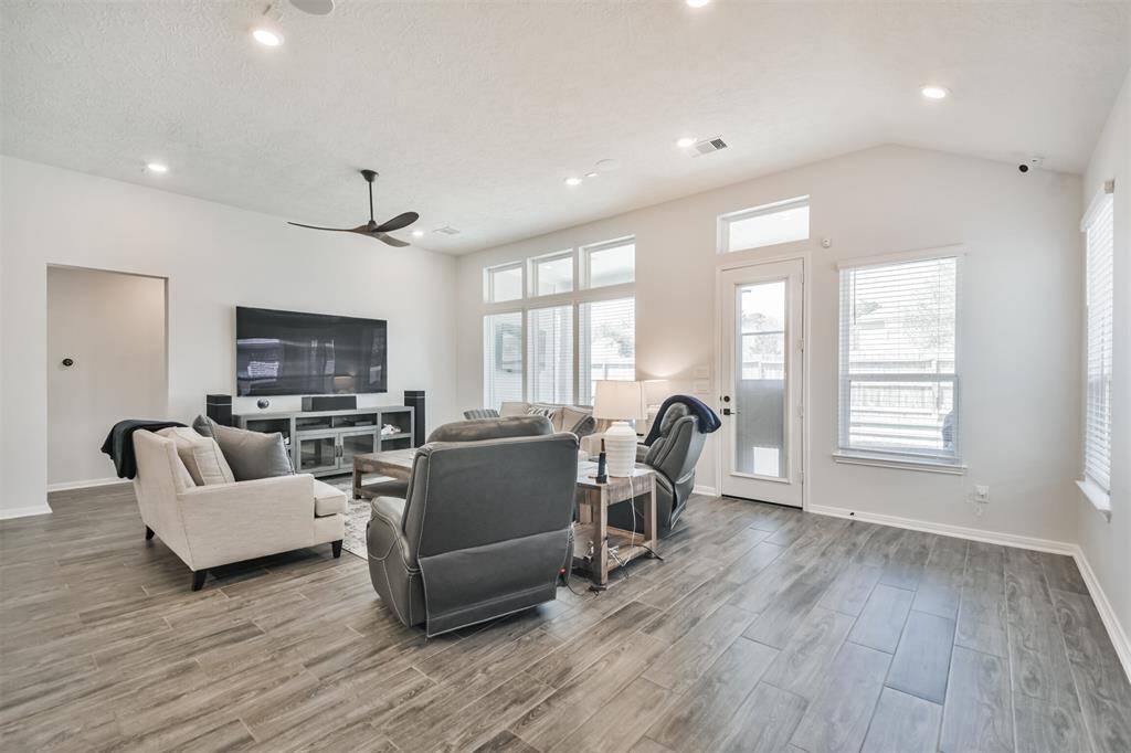 This spacious living room features modern wood-look flooring, ample natural light through large windows, and a sleek ceiling fan.